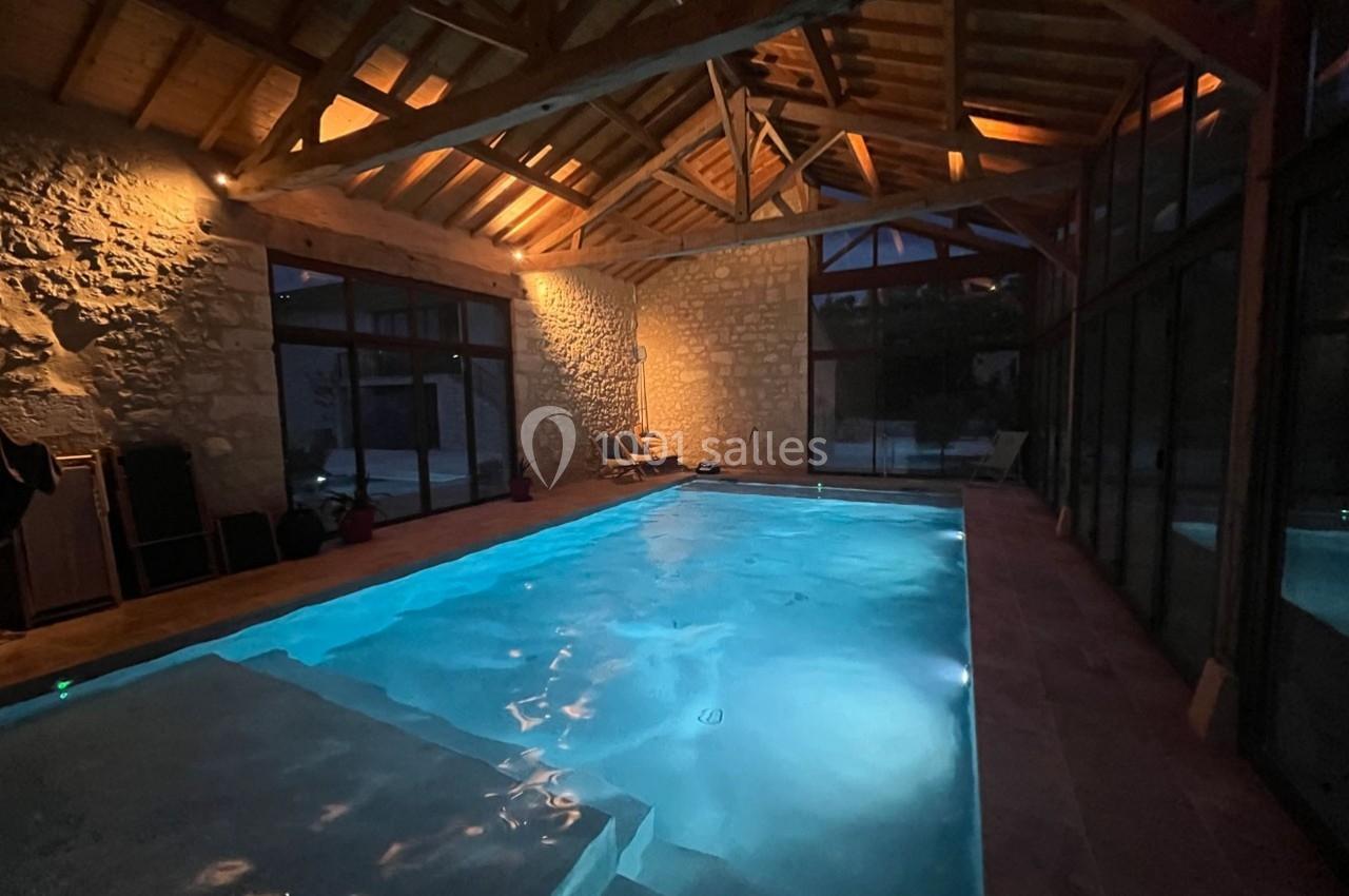 Piscine intérieure éclairée dans une pièce aux murs en pierre et charpente en bois, avec baies vitrées donnant sur l…
