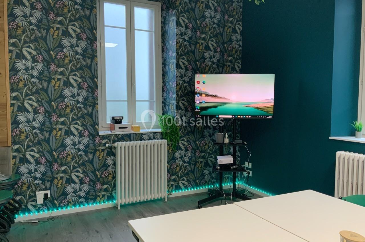 Salle équipée d'un écran sur support mobile, murs décorés de papier peint tropical et éclairage LED au sol.