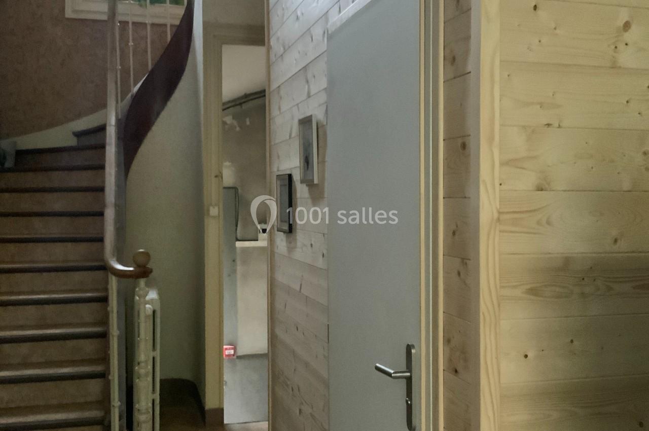 Escalier en bois courbé à côté d'une cabine en bois clair avec une porte blanche, dans un intérieur lumineux.