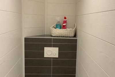 Toilettes modernes avec murs en bois clair, étagère intégrée contenant des produits ménagers dans un panier tressé.