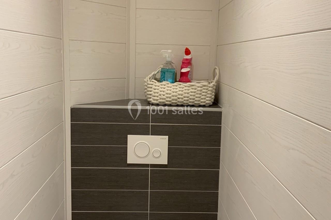 Toilettes modernes avec murs en bois clair, étagère intégrée contenant des produits ménagers dans un panier tressé.