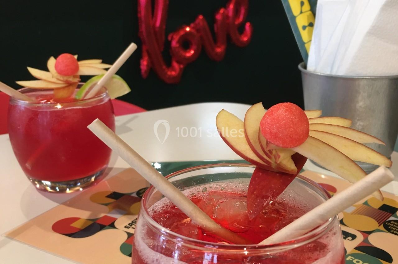 Deux verres de cocktail rouge décorés de tranches de pomme et de pastèque sur une table dans un café.