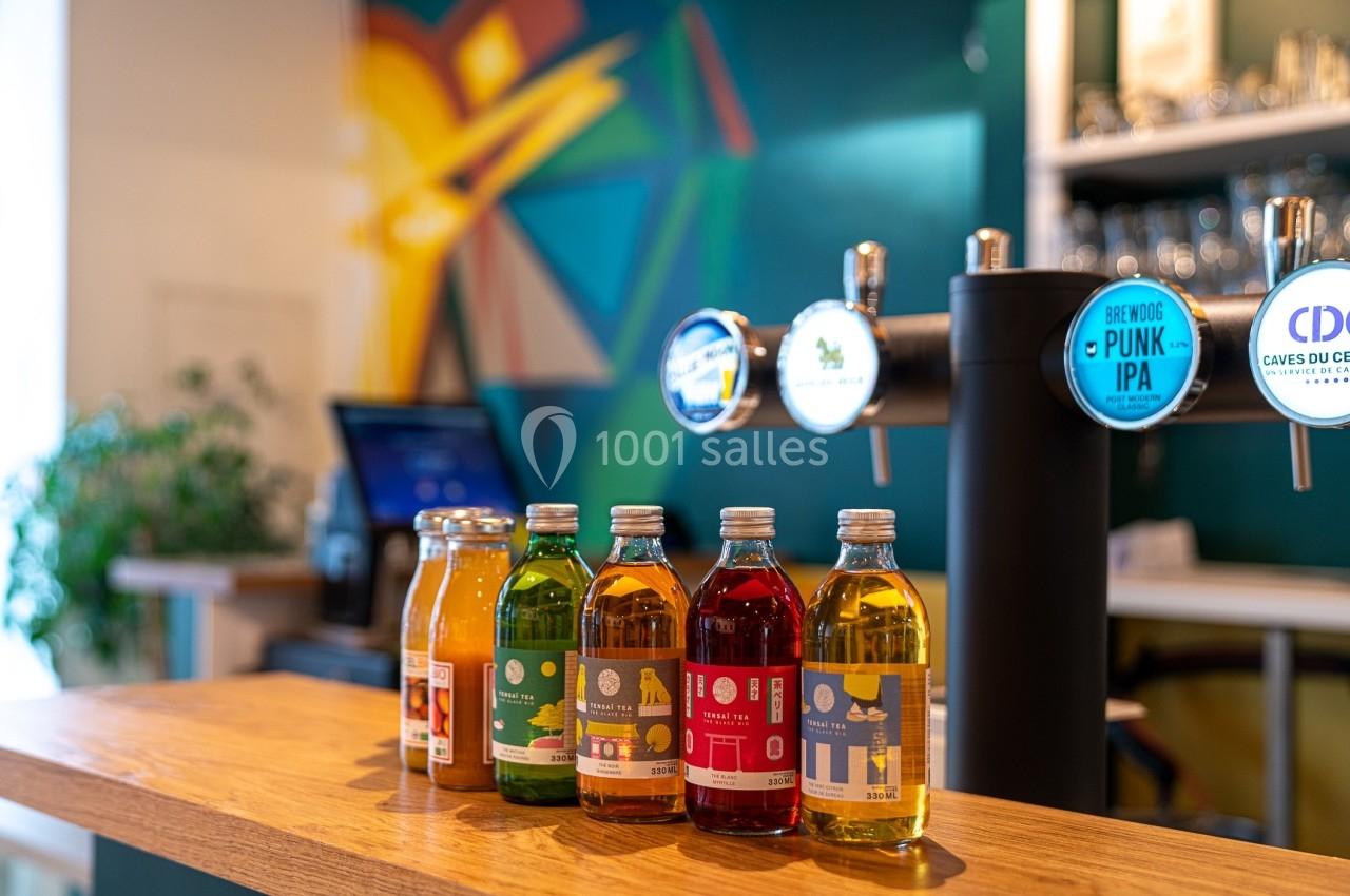 Bouteilles de boissons colorées alignées sur un comptoir en bois, avec des tireuses à bière et un décor moderne en arrière…