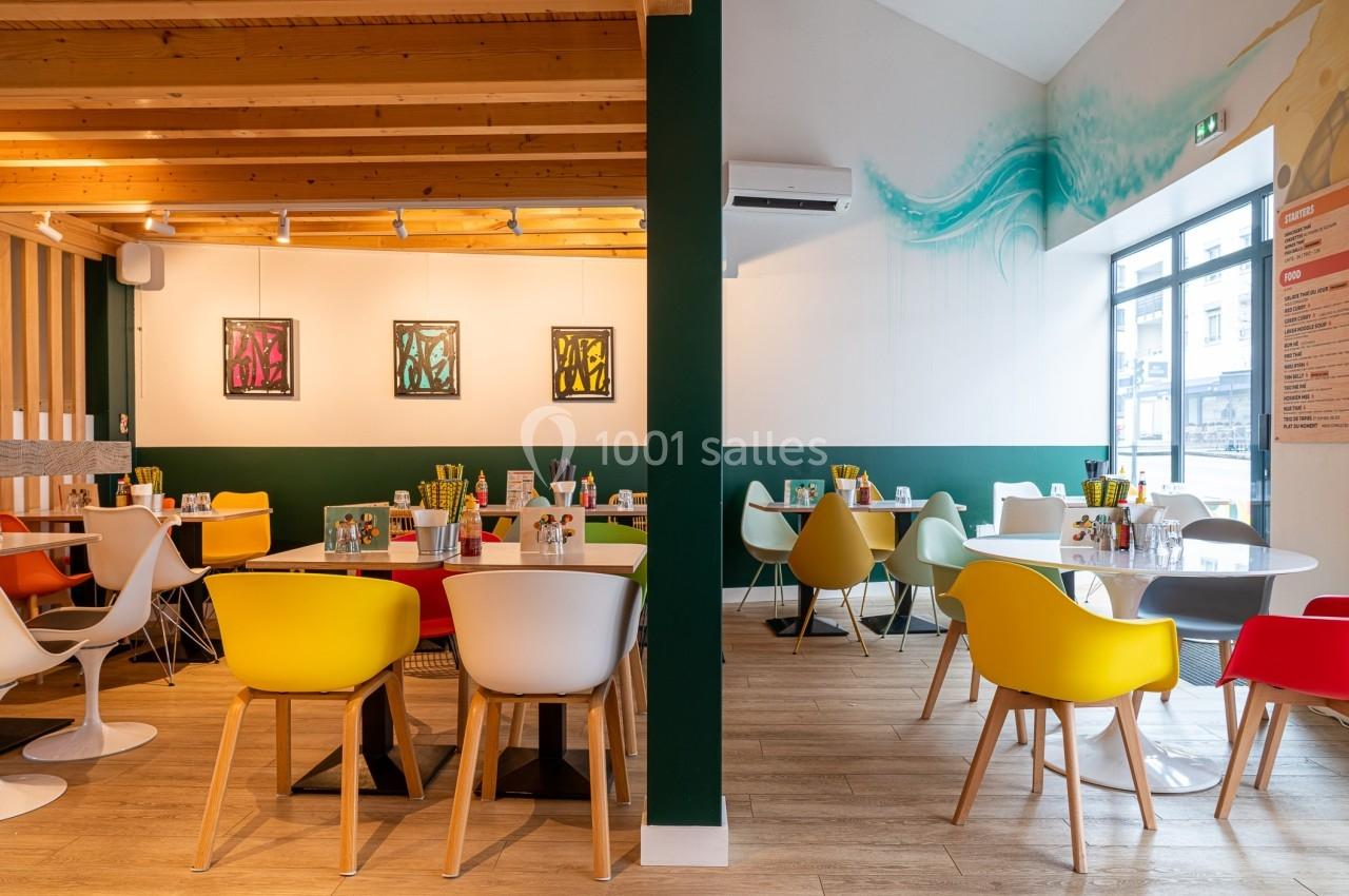 Salle de restaurant moderne avec des tables dressées, des chaises colorées et une décoration murale artistique.