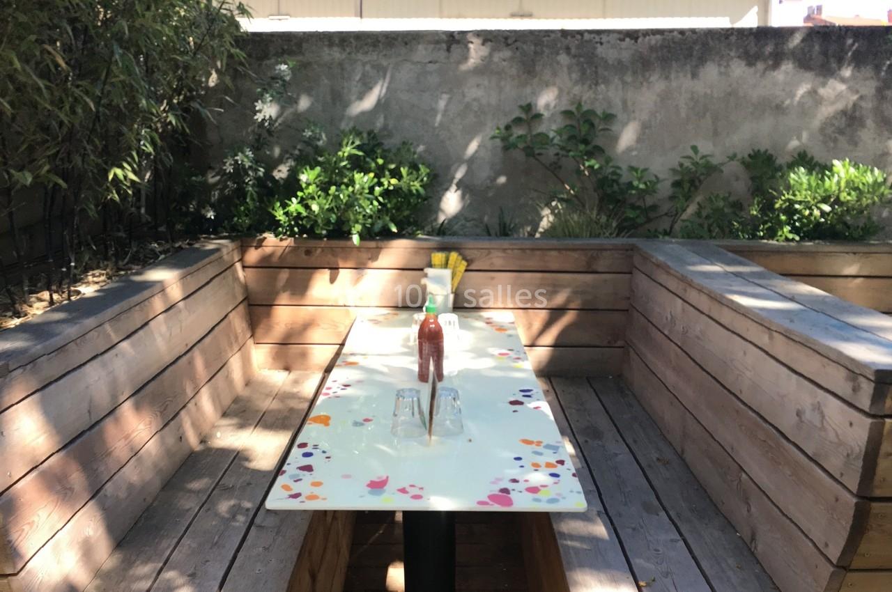 Table extérieure entourée de banquettes en bois, décorée de motifs colorés, avec condiments et verres posés dessus.