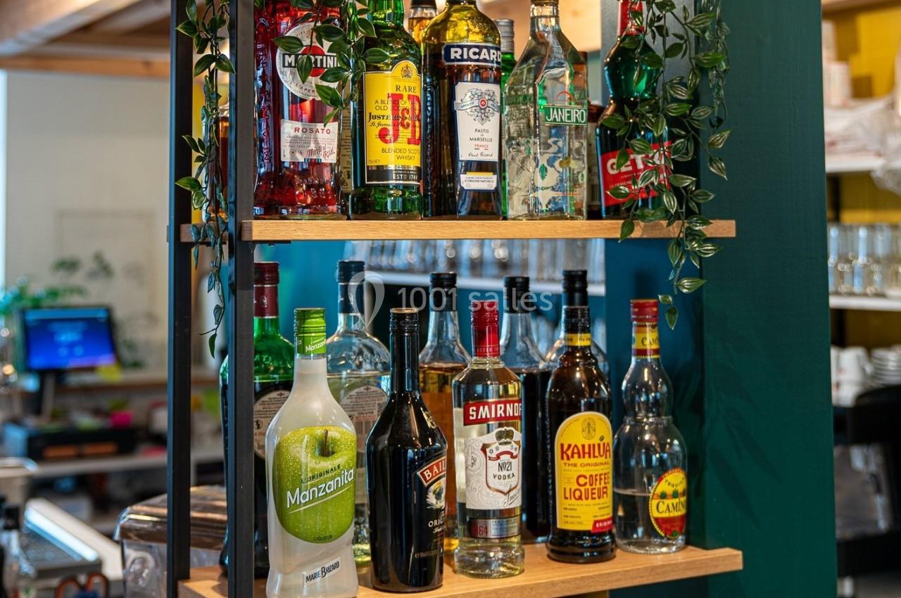 Bouteilles d'alcools variés disposées sur des étagères en bois dans un espace de bar ou restaurant.