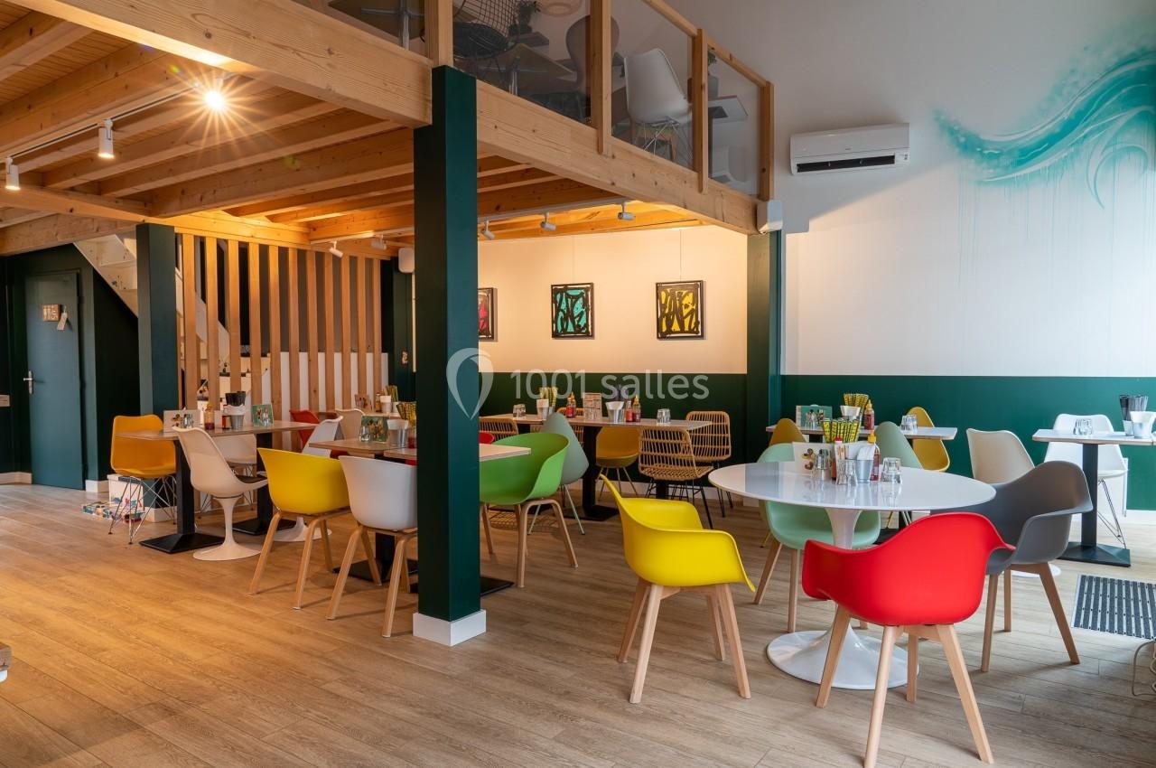 Salle de restaurant moderne avec mobilier coloré, parquet en bois clair et mezzanine en bois.