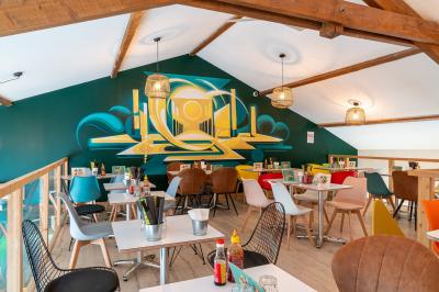 Vue d'un espace lumineux avec des chaises colorées autour d'une table, un comptoir d'accueil et des menus affichés au mur.