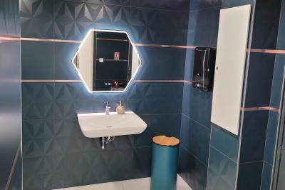 Réfrigérateur en acier inoxydable à double porte dans une pièce aux murs carrelés, avec une porte blanche ouverte.