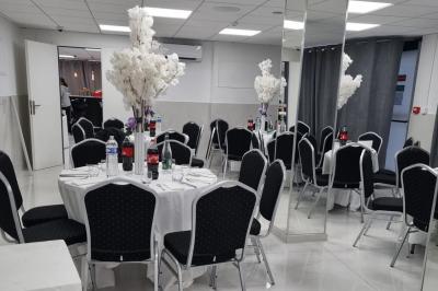 Réfrigérateur en acier inoxydable à double porte dans une pièce aux murs carrelés, avec une porte blanche ouverte.