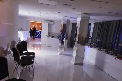 Réfrigérateur en acier inoxydable à double porte dans une pièce aux murs carrelés, avec une porte blanche ouverte.