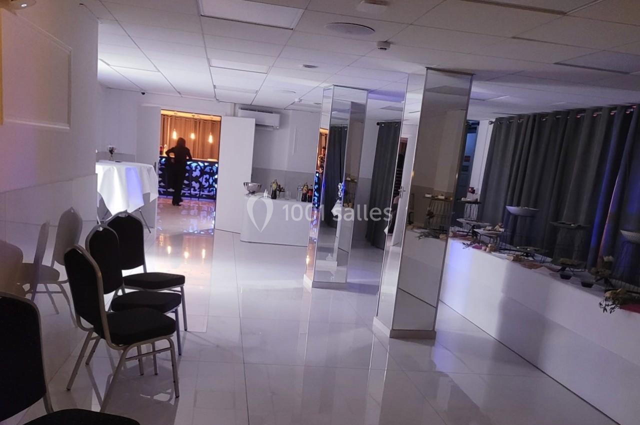 Salle lumineuse avec sol en carrelage blanc, tables dressées, chaises alignées et rideaux gris en arrière-plan.