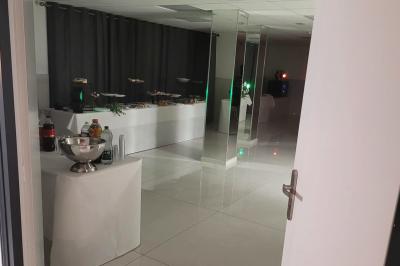 Réfrigérateur en acier inoxydable à double porte dans une pièce aux murs carrelés, avec une porte blanche ouverte.