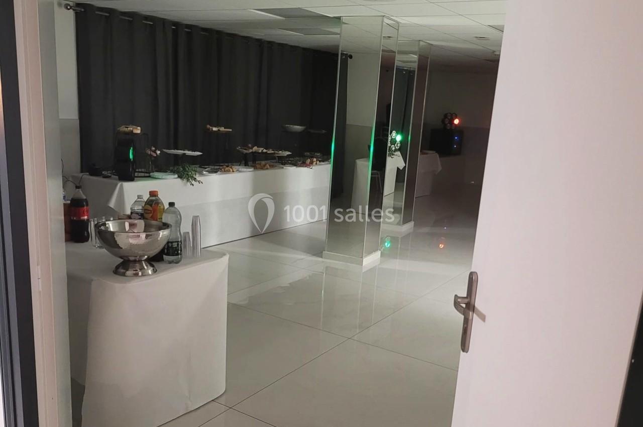 Salle lumineuse avec tables dressées pour un buffet, boissons et plats disposés, rideaux sombres en arrière-plan.