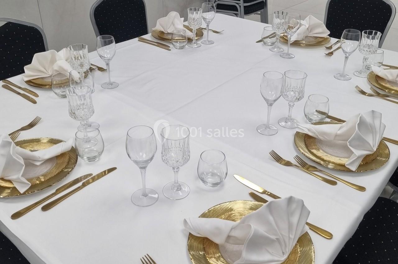 Table dressée avec nappes blanches, assiettes dorées, serviettes pliées, couverts dorés et verres en cristal.