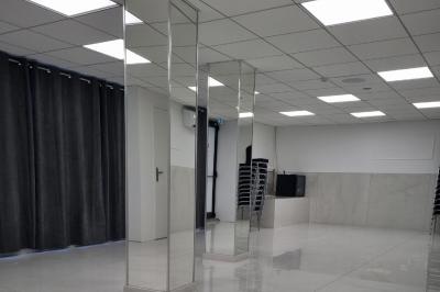 Réfrigérateur en acier inoxydable à double porte dans une pièce aux murs carrelés, avec une porte blanche ouverte.