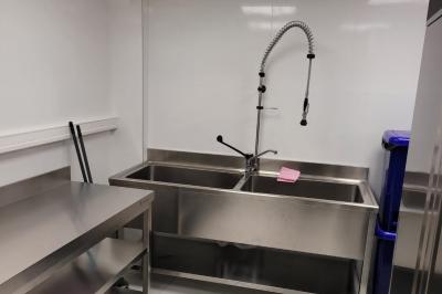 Réfrigérateur en acier inoxydable à double porte dans une pièce aux murs carrelés, avec une porte blanche ouverte.