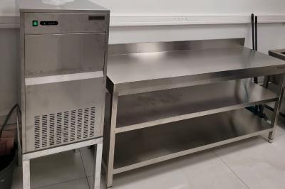 Réfrigérateur en acier inoxydable à double porte dans une pièce aux murs carrelés, avec une porte blanche ouverte.