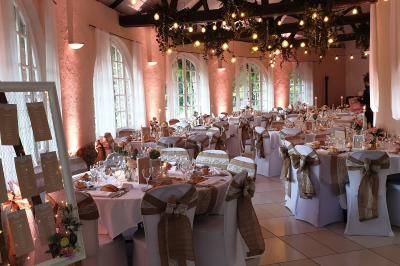 Des invités dansent autour de la mariée tenant des rubans colorés sous des guirlandes lumineuses dans une salle festive.