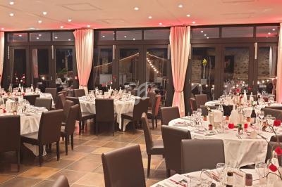 Salle de réception élégante avec tables rondes dressées, nappes blanches et décorations florales rouges.