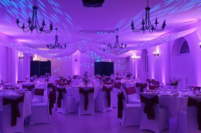 Salle de réception élégante avec tables rondes dressées, nappes blanches et décorations florales rouges.