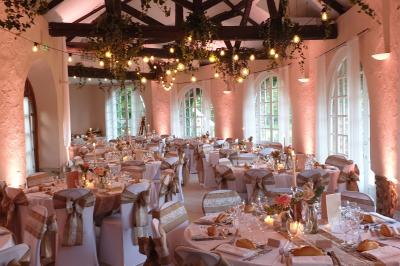Salle de réception élégante avec tables rondes dressées, nappes blanches et décorations florales rouges.