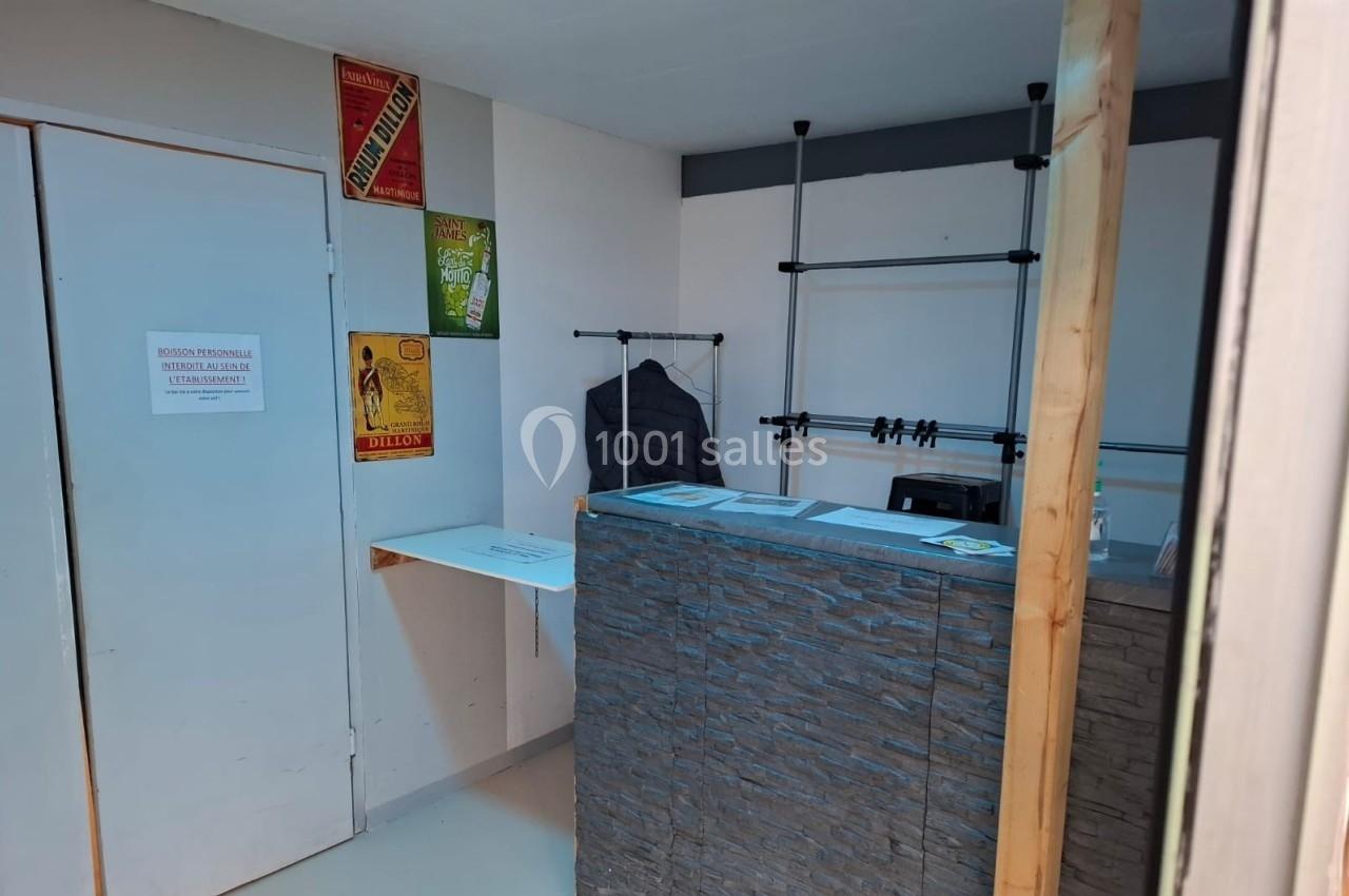 Comptoir en pierre avec porte-manteaux, affiches au mur et porte blanche dans une pièce lumineuse.