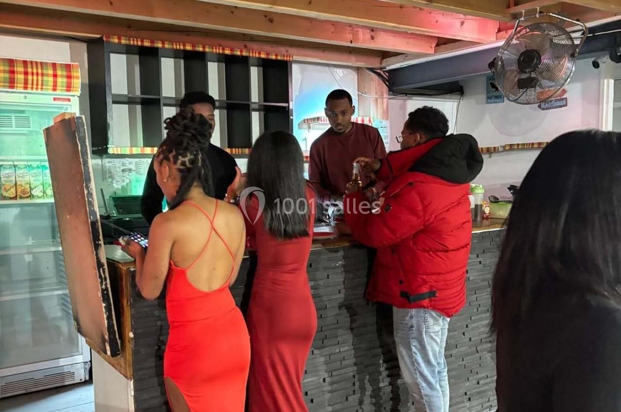 Des personnes discutent et commandent au comptoir d'un bar, dans un espace intérieur avec une ambiance décontractée.