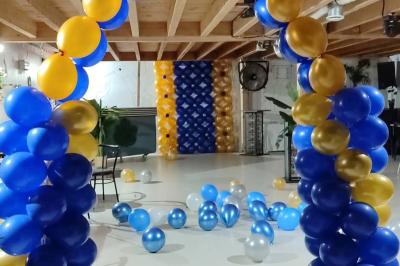 Salle décorée pour une fête avec une longue table dressée, bougies, confettis et ballons dorés.