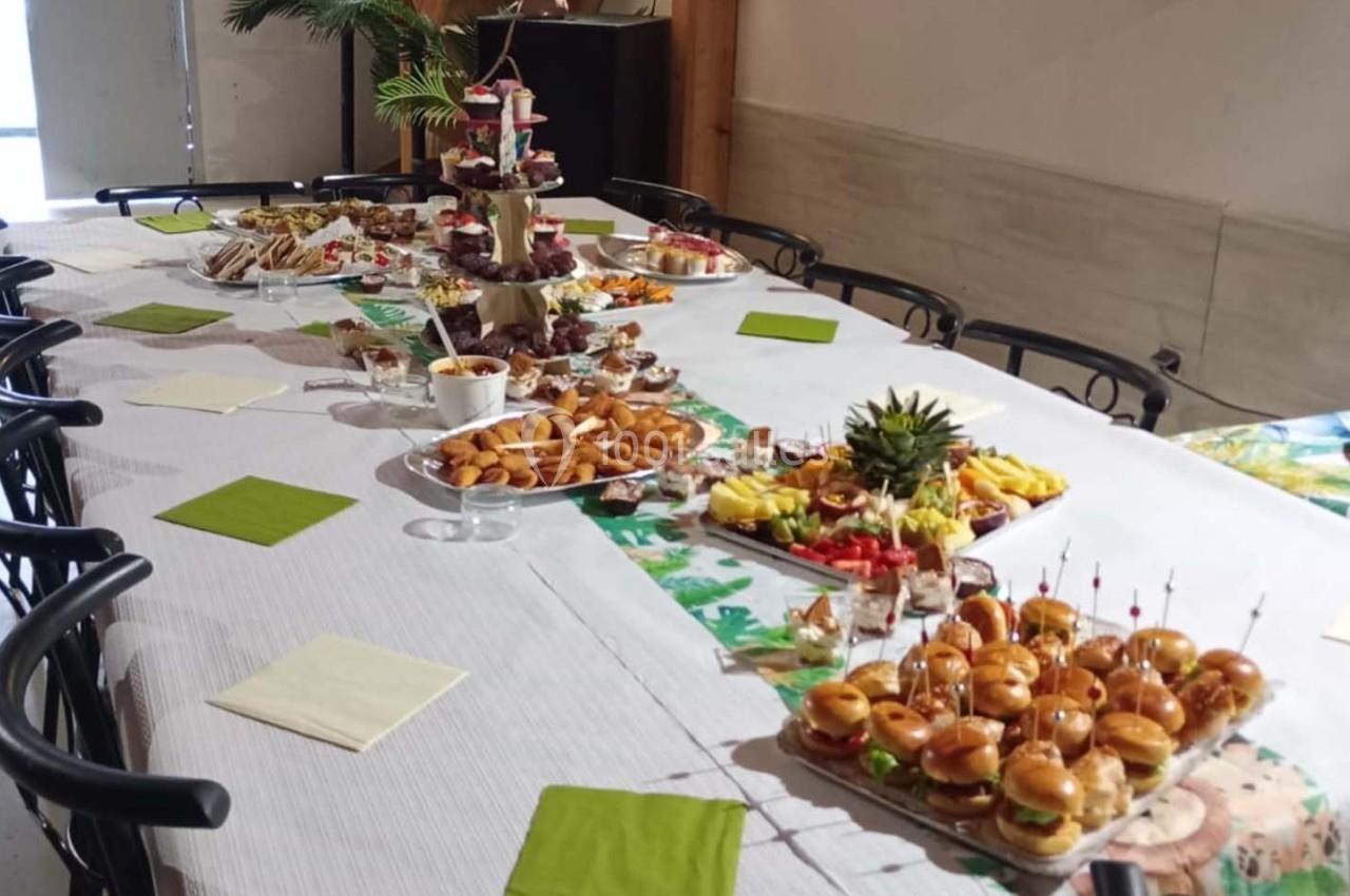 Table dressée avec un buffet varié comprenant mini-burgers, fruits, viennoiseries et desserts, dans une salle lumineuse.
