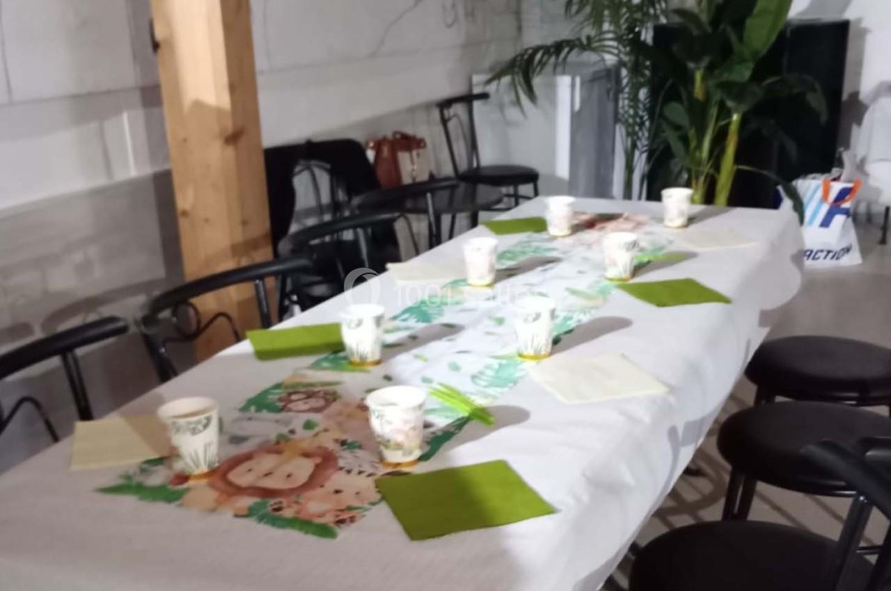 Table dressée avec une nappe blanche, des serviettes vertes, des gobelets décorés et un chemin de table à motifs d'animaux.