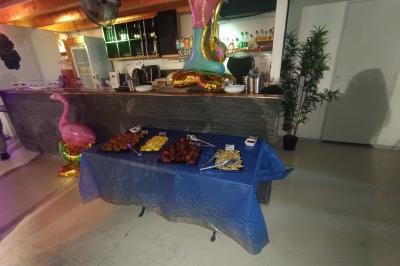 Salle décorée pour une fête avec une longue table dressée, bougies, confettis et ballons dorés.
