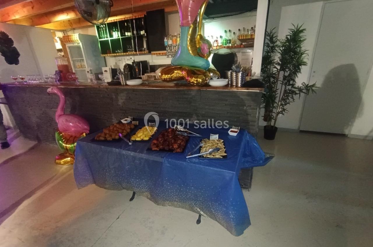 Buffet avec divers amuse-bouches disposés sur une table bleue, dans un espace décoré avec des ballons et des plantes.
