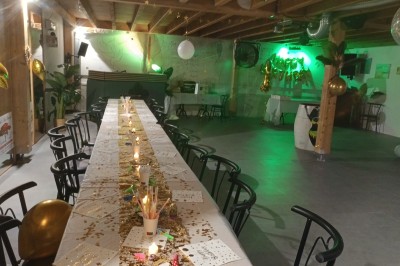 Salle décorée pour une fête avec une longue table dressée, bougies, confettis et ballons dorés.