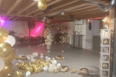 Salle décorée pour une fête avec guirlandes lumineuses, sapin de Noël et tables alignées sous un plafond en bois.