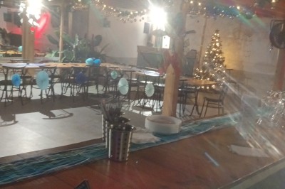 Salle décorée pour une fête avec guirlandes lumineuses, sapin de Noël et tables alignées sous un plafond en bois.