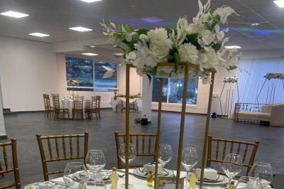 Salle de réception élégamment décorée avec des tables rondes, des chaises dorées et blanches, et des arrangements floraux.