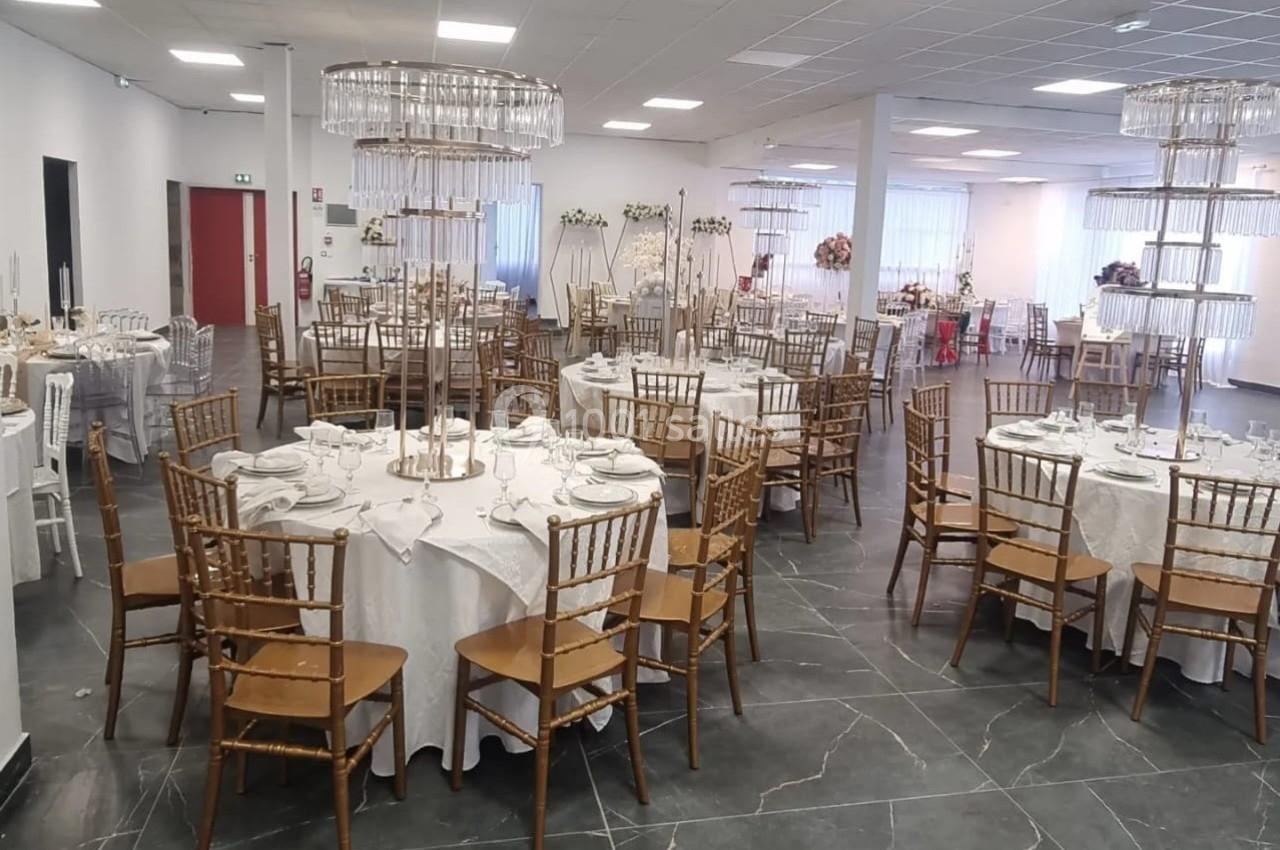 Salle de réception décorée avec des tables rondes dressées, chaises en bois et centres de table ornés de bougies.