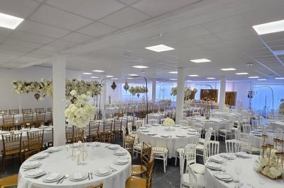 Salle de réception élégamment décorée avec des tables rondes, des chaises dorées et blanches, et des arrangements floraux.