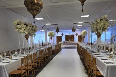 Salle de réception élégamment décorée avec des tables rondes, des chaises dorées et blanches, et des arrangements floraux.