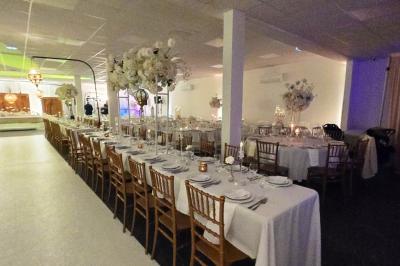 Salle de réception élégamment décorée avec des tables rondes, des chaises dorées et blanches, et des arrangements floraux.