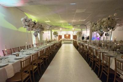 Salle de réception élégamment décorée avec des tables rondes, des chaises dorées et blanches, et des arrangements floraux.