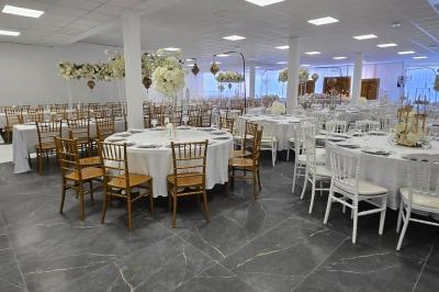Salle de réception élégamment décorée avec des tables rondes, des chaises dorées et blanches, et des arrangements floraux.