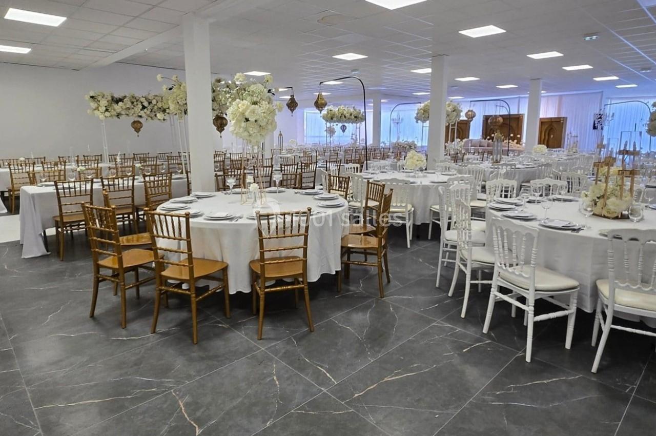 Salle de réception élégamment décorée avec des tables rondes, des chaises dorées et blanches, et des arrangements floraux.