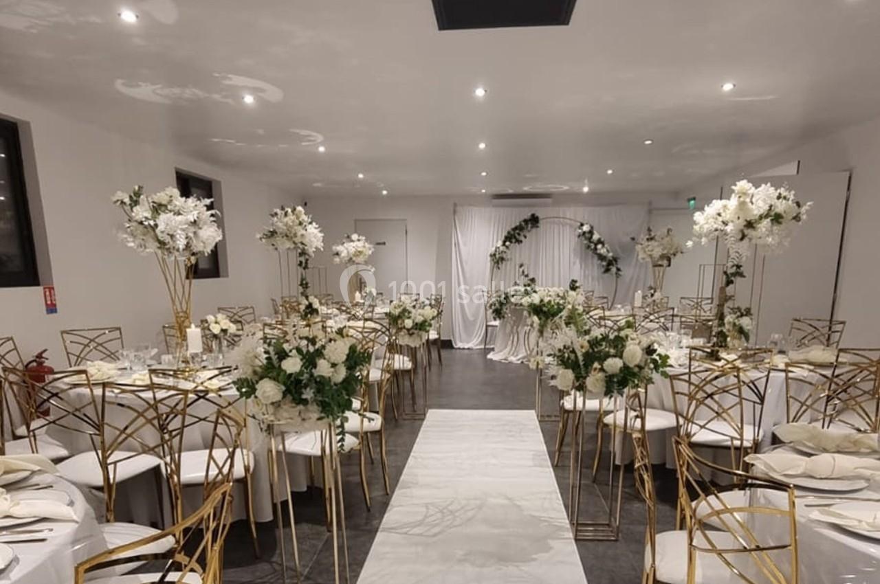 Salle de réception décorée avec des tables rondes, des chaises dorées et des arrangements floraux blancs.