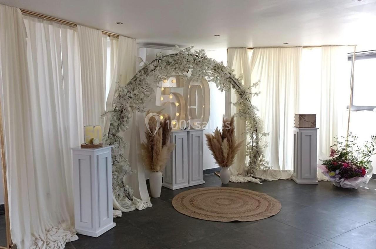 Décoration intérieure avec arche florale, chiffres ’50’, colonnes blanches et arrangements de fleurs séchées.