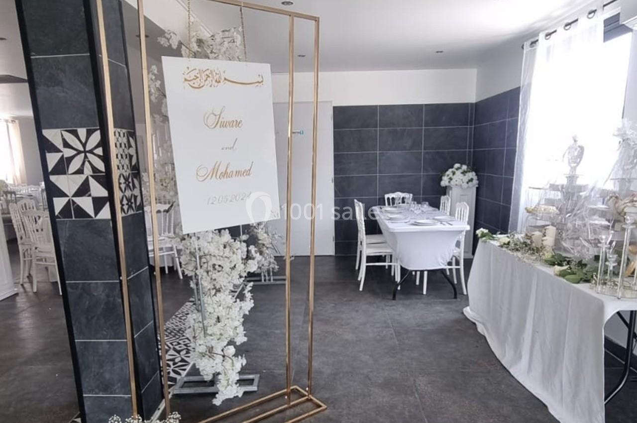 Décoration de salle avec panneau de mariage, fleurs blanches et table dressée dans un espace moderne et lumineux.