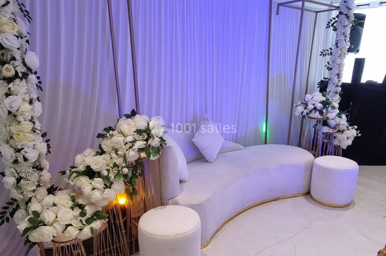 Canapé blanc entouré de fleurs blanches et de rideaux, décoré pour un événement ou une cérémonie.