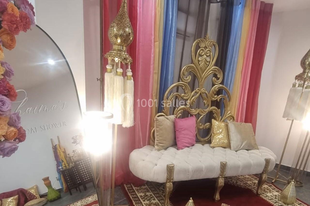 Canapé blanc capitonné avec dossier doré orné, entouré de rideaux colorés et de décorations orientales dorées.