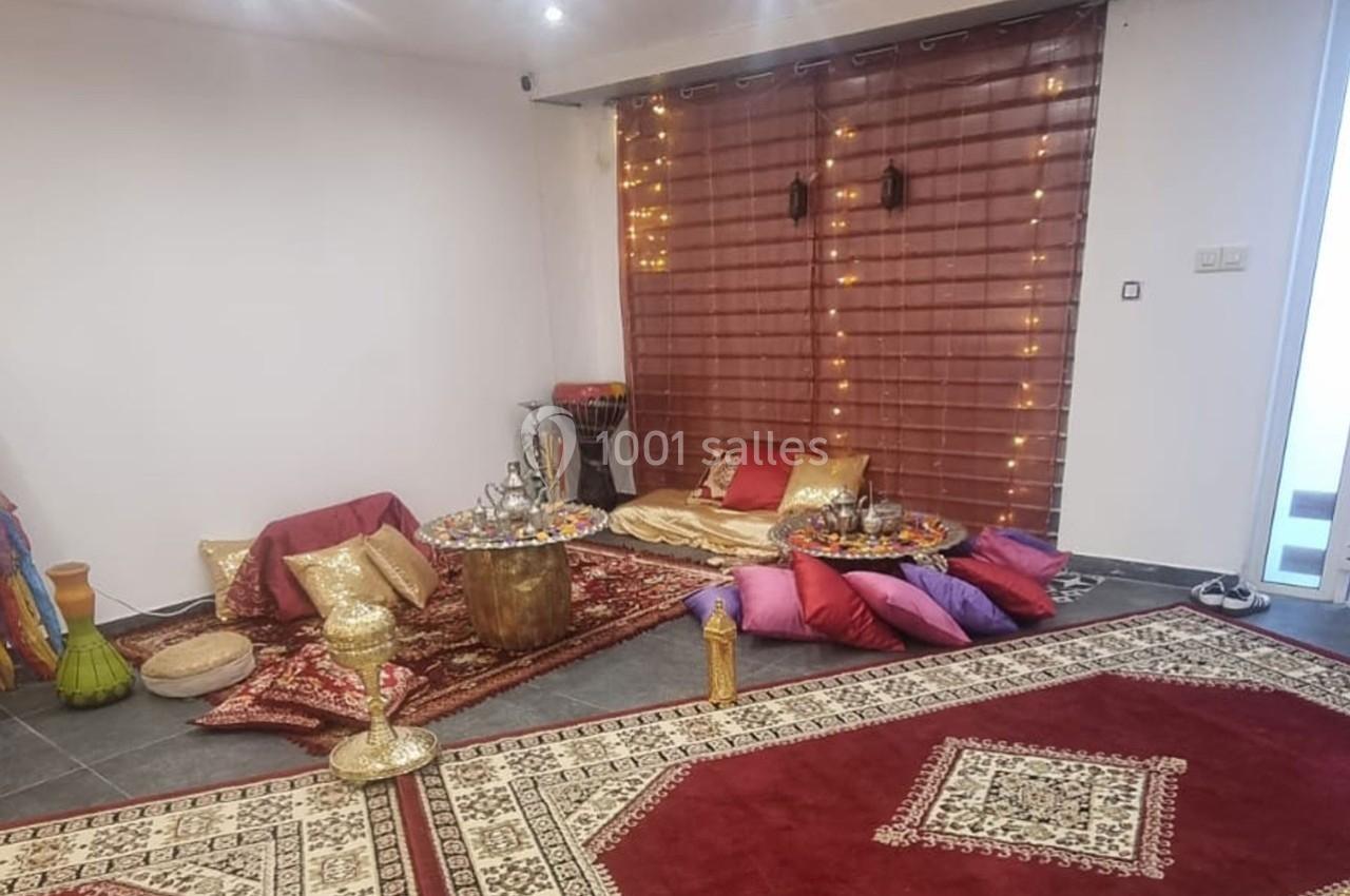 Espace décoré avec tapis, coussins colorés, tables basses et objets orientaux, devant un rideau illuminé.